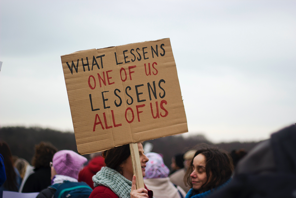 What lessens one of us lessens all of us - sign in a protest